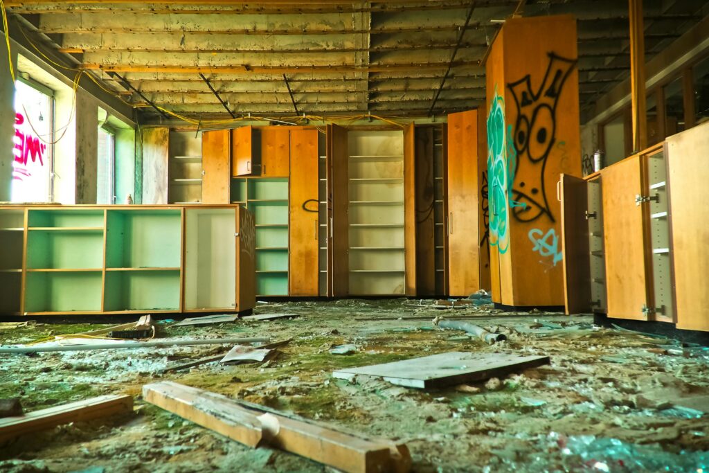 Explore a neglected, graffiti-filled room with dilapidated cabinets and broken furniture.